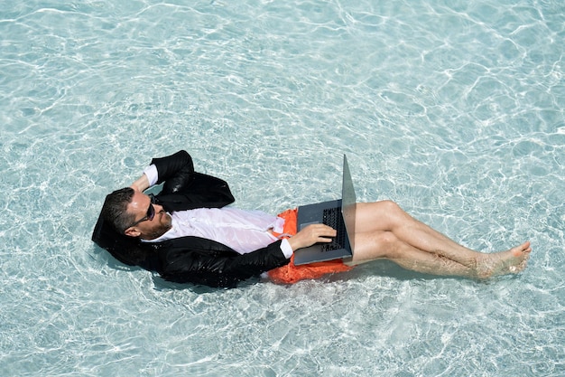 Gracioso hombre de negocios en traje trabajando con computadora en la playa de mar vacaciones de verano al aire libre y negocios