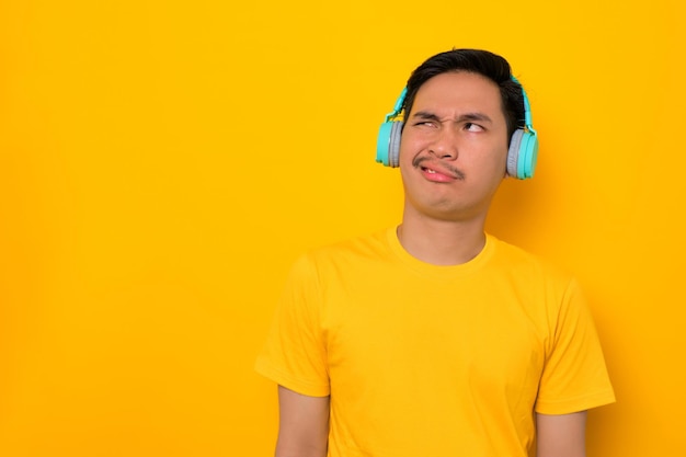 Gracioso joven asiático en camiseta casual escuchando música en auriculares mirando hacia otro lado en el espacio de copia aislado sobre fondo amarillo Personas emociones concepto de estilo de vida