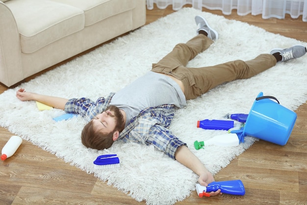 Gracioso joven cansado de limpiar alfombras en casa