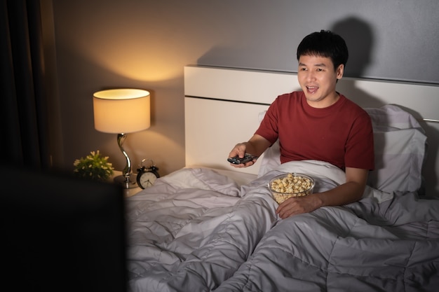 Gracioso joven viendo la televisión y riendo en una cama por la noche