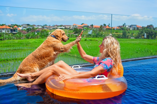 Gracioso labrador retriever dorado choca los cinco con la niña feliz nadando en la piscina. diversión en fiesta en la piscina en villa de lujo.