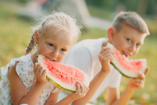 Gracioso niño pequeño niños hermano y hermana comiendo sandía en el parque. Niño y niña felices juntos. Infancia, familia, concepto de dieta saludable.