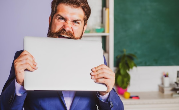 Gracioso profesor con portátil en el aula en la escuela emocionado profesor profesor vistiendo formal s