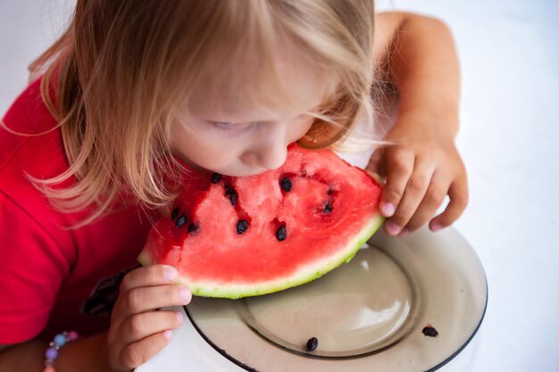 Gracioso retrato de niño rubio con sandía en el interior ver hacia arriba Bonita niña pequeña de 4 años comiendo sandía closeup