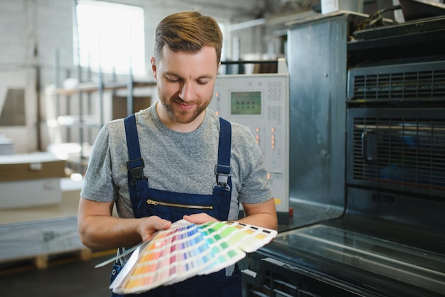 Gracioso retrato de tipógrafo de pie con muestras de color en la fabricación de impresión