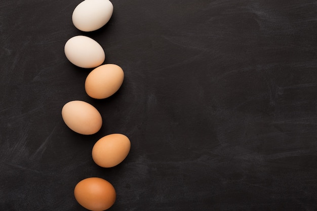 Gradiente de huevos de colores naturales dispuestos en fila sobre fondo negro. Tarjeta de felicitación de Pascua minimalista o publicidad de comidas orgánicas, vista superior, espacio de copia