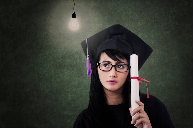 Foto graduada atractiva con certificado y bombilla encendida