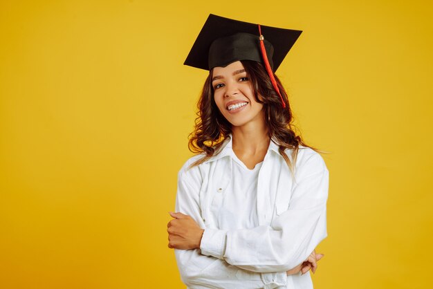 Graduada mulher com um chapéu de formatura na cabeça posando em amarelo