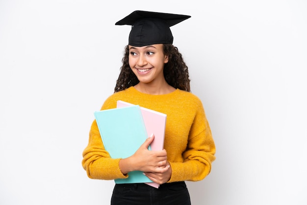 Graduada de la universidad árabe mujer sosteniendo libros aislado sobre fondo blanco mirando hacia el lado