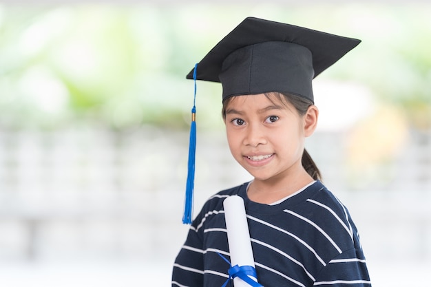 Graduado de criança de escola feminina asiática feliz retrato em um chapéu de formatura detém um certificado laminado. Conceito de celebração da graduação Foto de stock