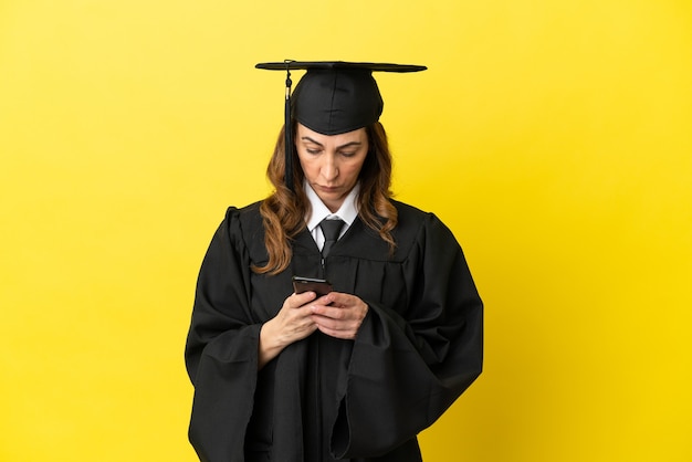 Graduado de meia-idade isolado em um fundo amarelo, enviando uma mensagem com o celular