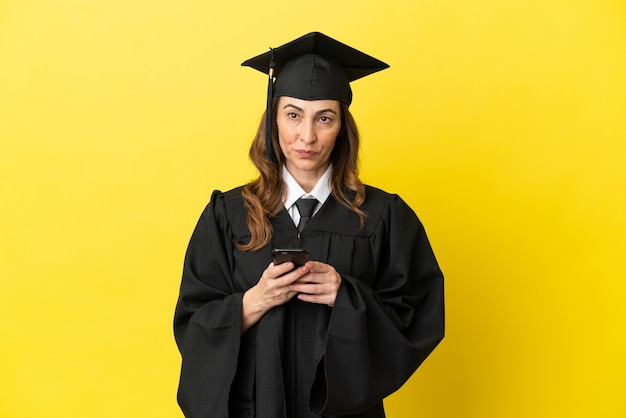 Graduado de meia-idade isolado em um fundo amarelo, enviando uma mensagem com o celular