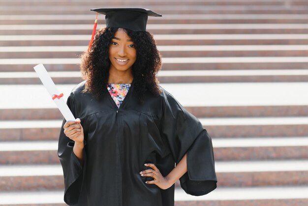 Graduado femenino afroamericano alegre de pie delante del edificio de la universidad