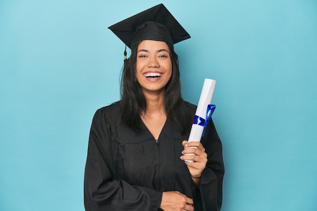 Foto graduado filipino com diploma no estúdio azul rindo e se divertindo