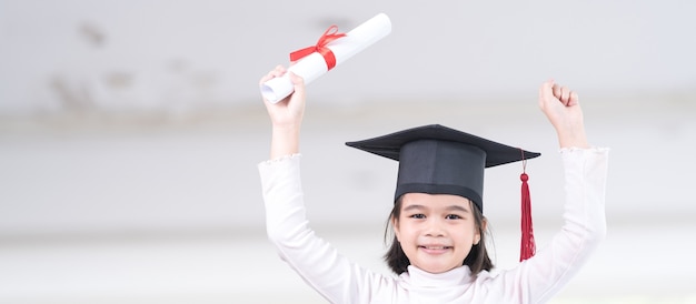 Graduado de niño de escuela asiática femenina con un gorro de graduación tiene un papel de certificado enrollado