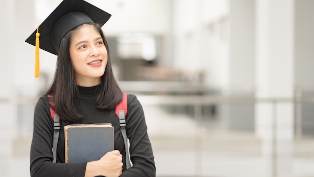 Graduado universitário jovem feliz mulher asiática em vestido de formatura e boné no campus da faculdade. Foto de estoque de educação