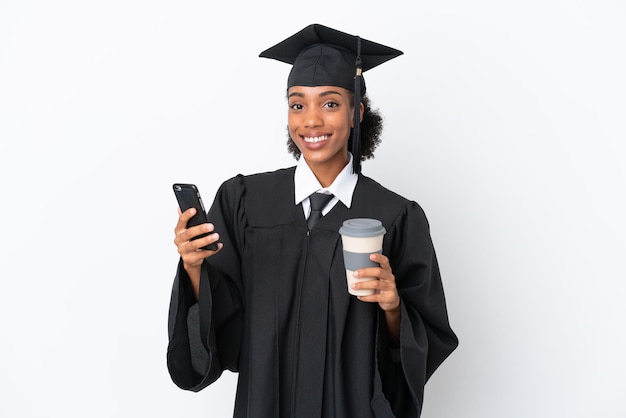 Graduado universitario joven afroamericana aislada sobre fondo blanco sosteniendo café para llevar y un móvil