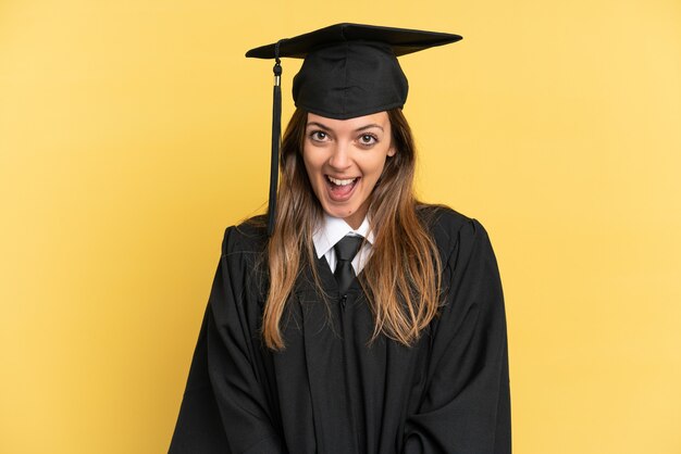 Graduado universitario joven aislado sobre fondo amarillo con expresión facial sorpresa