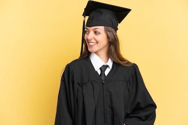 Graduado universitario joven aislado sobre fondo amarillo mirando hacia el lado