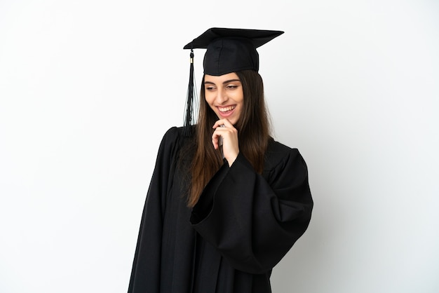 Graduado universitario joven aislado sobre fondo blanco mirando hacia el lado y sonriendo