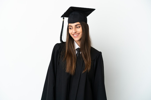 Graduado universitario joven aislado sobre fondo blanco mirando hacia el lado y sonriendo