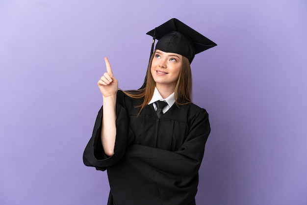 Graduado universitario joven sobre fondo púrpura aislado apuntando hacia una gran idea