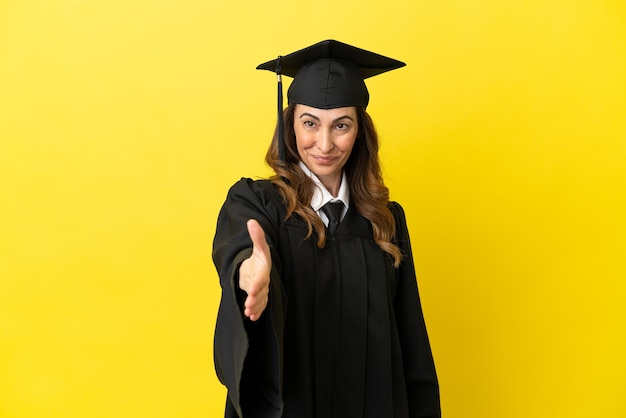 Graduado universitario de mediana edad aislado sobre fondo amarillo un apretón de manos para cerrar un buen trato