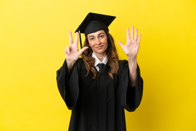 Graduado universitario de mediana edad aislado sobre fondo amarillo contando ocho con los dedos