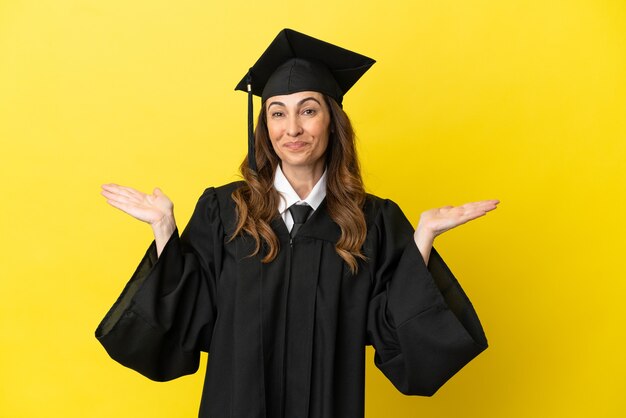 Graduado universitario de mediana edad aislado sobre fondo amarillo con expresión facial sorprendida