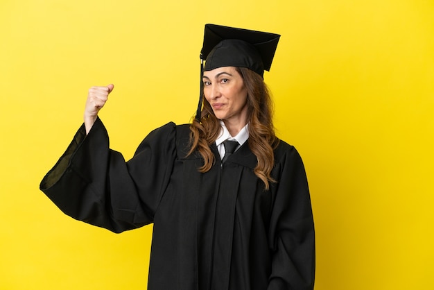 Graduado universitario de mediana edad aislado sobre fondo amarillo haciendo gesto fuerte