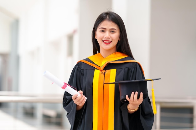 Graduados segurando chapéus pretos com borlas amarelas em pé com diploma levantado na mão sobre o pôr do solCongratulação da educação do conceito Cerimônia de formatura Felicitou os graduados na universidade