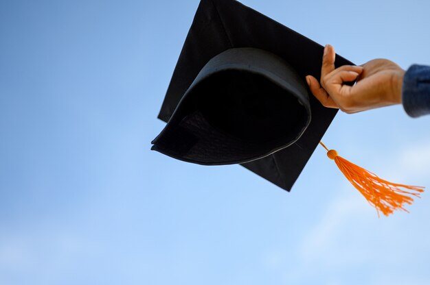 Los graduados sostienen un sombrero negro con una borla amarilla unida al cielo.