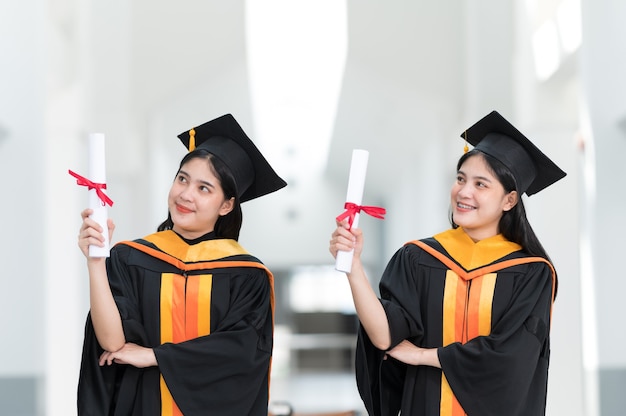 Graduados universitarios femeninos con sombreros negros, borlas amarillas, sonrientes y felices el día de la graduación