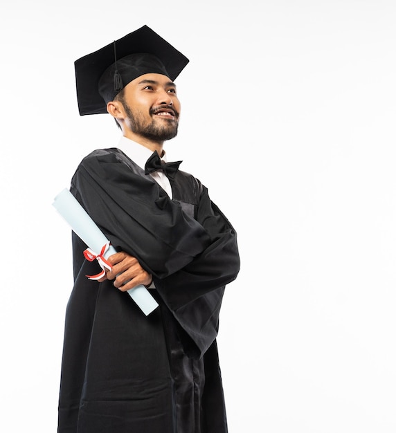 Foto graduando homem vestindo uma toga com as mãos postas em pé segurando o papel do certificado em um fundo branco
