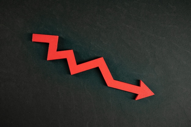 Foto gráfico com seta vermelha para baixo isolada no fundo preto. queda no crescimento dos negócios
