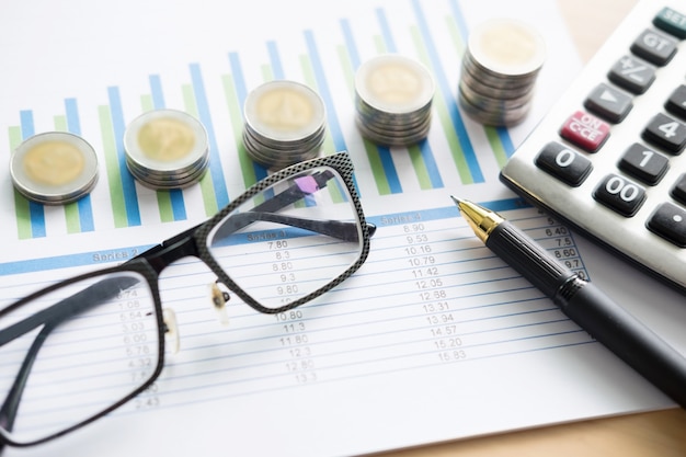 Gráficos financeiros na mesa com laptop, calculadora, caneta e conceito de negócios de óculos