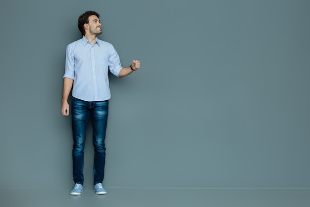 Gráficos virtuais. Homem bonito e alegre sorrindo e segurando um objeto virtual em pé contra um fundo cinza