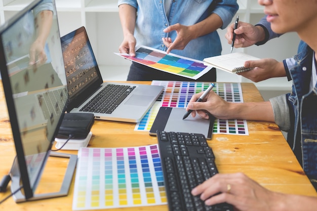 Grafikdesigner-Team, das an Webdesign unter Verwendung der Farbmuster, die Grafik unter Verwendung der Tablette und eines Stiftes bearbeiten, an den Schreibtischen im beschäftigten kreativen Büro bearbeitet.