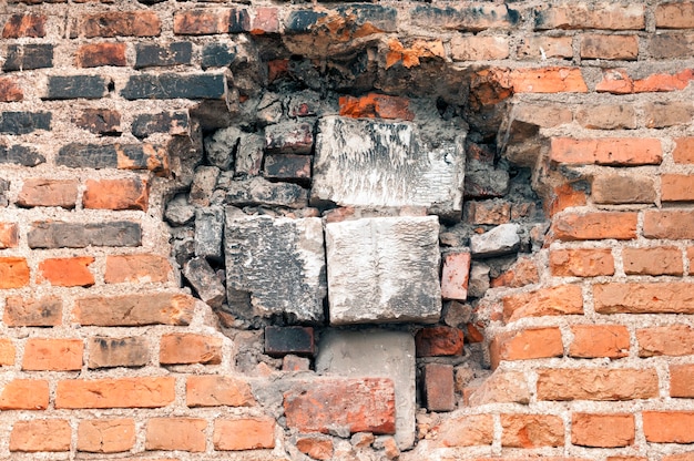 Gran agujero en la vieja pared de ladrillos rodeada de diferentes piezas de bloque