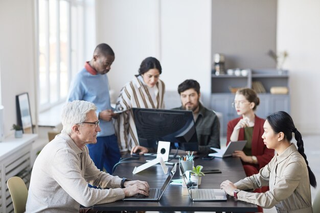 Gran angular en un grupo diverso de gente de negocios reunida en la oficina y usando la computadora mientras se discute el proyecto
