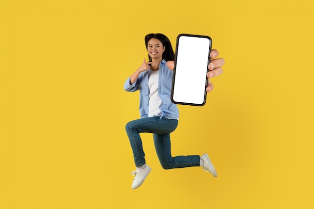 Gran anuncio de venta y oferta Feliz bastante joven estudiante coreana saltando apuntando con el dedo al teléfono