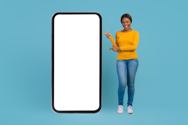 Gran aplicación hermosa mujer afroamericana apuntando a un gran teléfono móvil en blanco