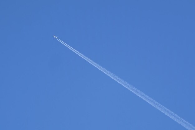 Foto gran avión de pasajeros volando alto en un cielo azul despejado sin nubes dejando una larga huella blanca