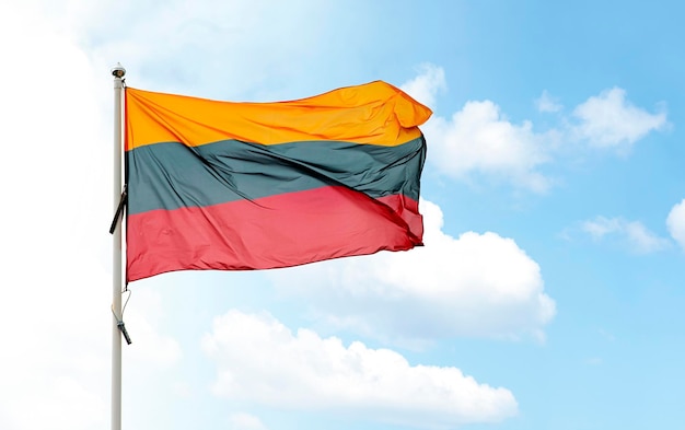Gran bandera nacional lituana en asta de bandera ondeando en el viento contra el cielo azul nublado