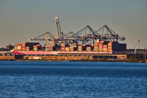 Gran barco lleno de contenedores de carga en la costa de la ciudad de Nueva York a la luz de la hora dorada