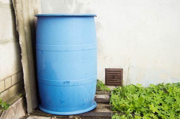 Foto un gran barril de agua de lluvia de plástico azul se encuentra afuera, cerca de la pared. se usa para regar.