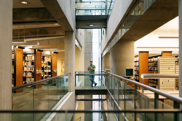 Gran biblioteca espaciosa con estanterías Estudiante atractivo que usa tecnología digital de tableta