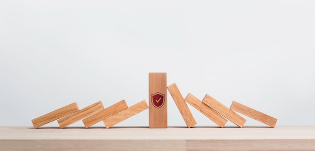 El gran bloque de madera fuerte con símbolo de icono de seguridad de escudo de pie entre piezas de dominó que caen aisladas sobre fondo blanco. Deteniendo el efecto dominó. Gestión de datos comerciales. Protección contra riesgos.