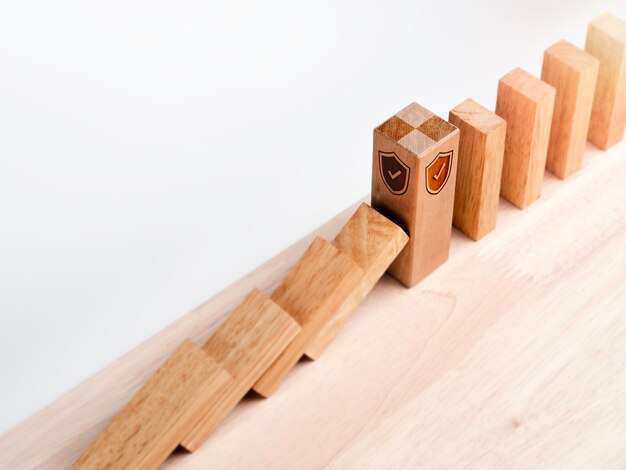 El gran bloque de madera fuerte con el símbolo del icono de seguridad del escudo de pie protege las piezas de dominó que caen aisladas en blanco. Deteniendo el efecto dominó. Gestión de datos comerciales. Protección contra riesgos.