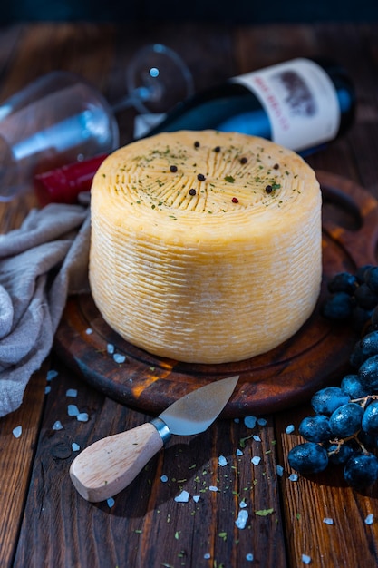 Gran cabeza de queso en una tabla de cortar con hierbas y uvas azules.